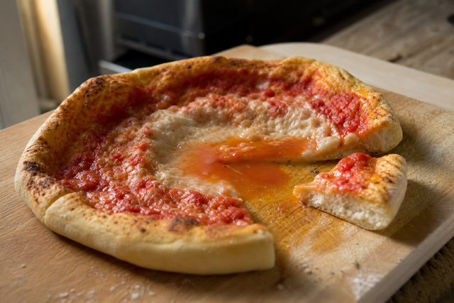 Pizza maison coupée en parts montrant un centre de pizza crue et un fond de pizza mou