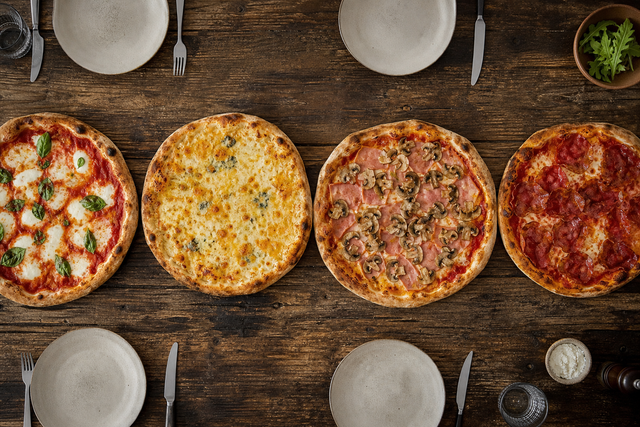 Quatre pizzas classiques vues de dessus sur une table en bois : margherita, quatre fromages, jambon-champignons et charcuterie