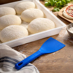 Pâtons de pizza farinés et spatule souple bleue sur un plan de travail
