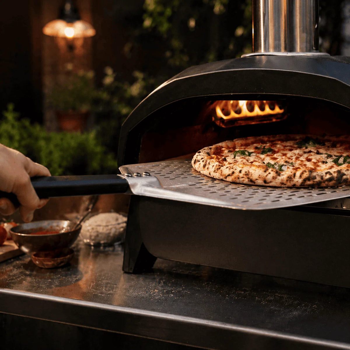 Enfournement d'une pizza crue avec la pelle à pizza perforée dans un four à pizza